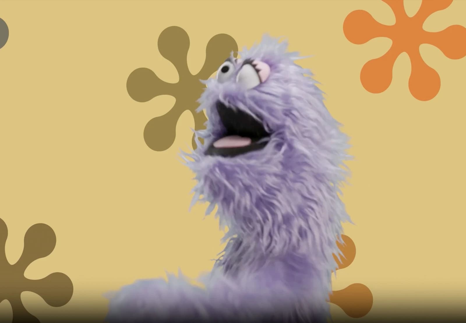 Lavender character asset showing a fluffy purple puppet looking upward with an expressive open mouth on a retro-styled yellow background.